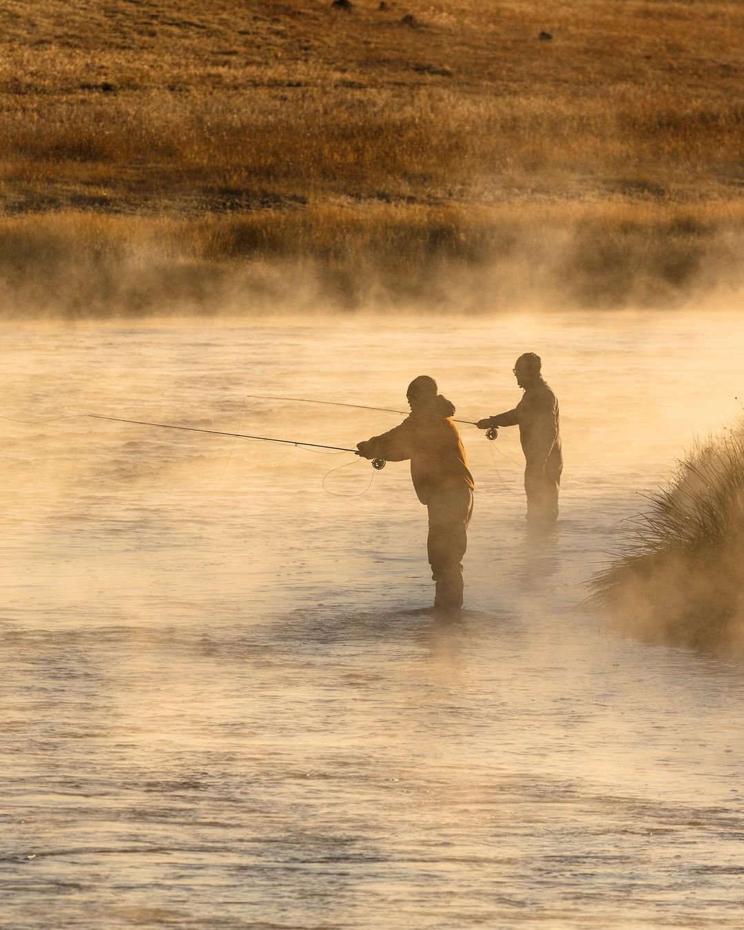 Deux pêcheurs à la mouche dans la brume dorée d'une rivière, au lever du soleil